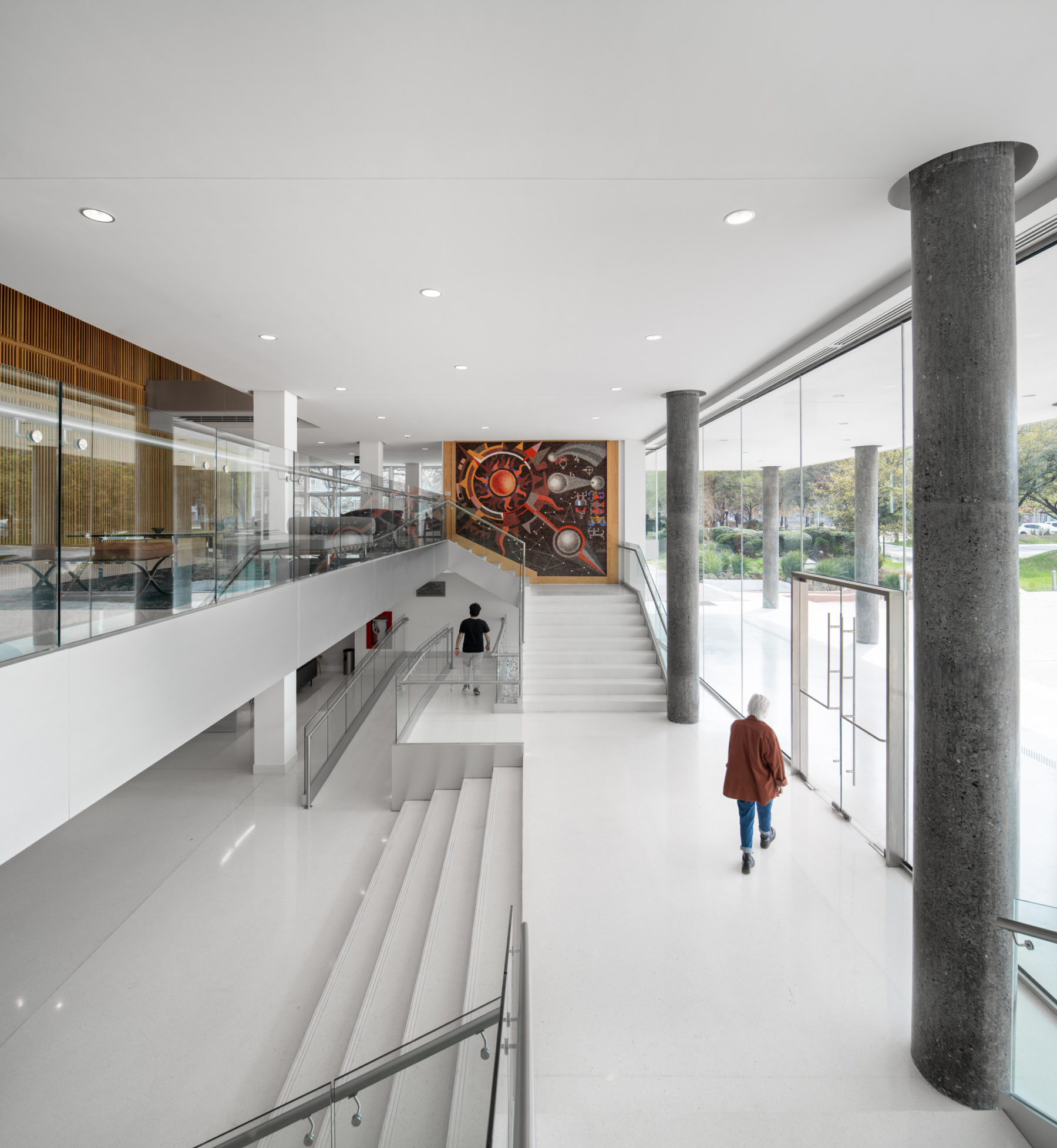 Interior photo of building entry from a side angle. A person walks towards the exit in the foreground, another walks down the ramp in the background